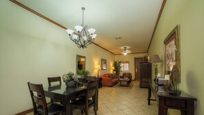 A dining area with a dark wooden table and chairs, a chandelier, and a living room with a sofa and lamp. - Veranda 4F 2 bdr Garden View in Los Suenos (Playa Herradura)