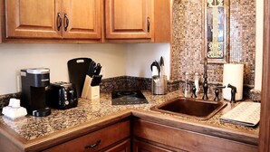 A kitchen with wooden cabinets, a granite countertop, a coffee maker, a toaster, a knife block, and a sink with a decorative faucet.