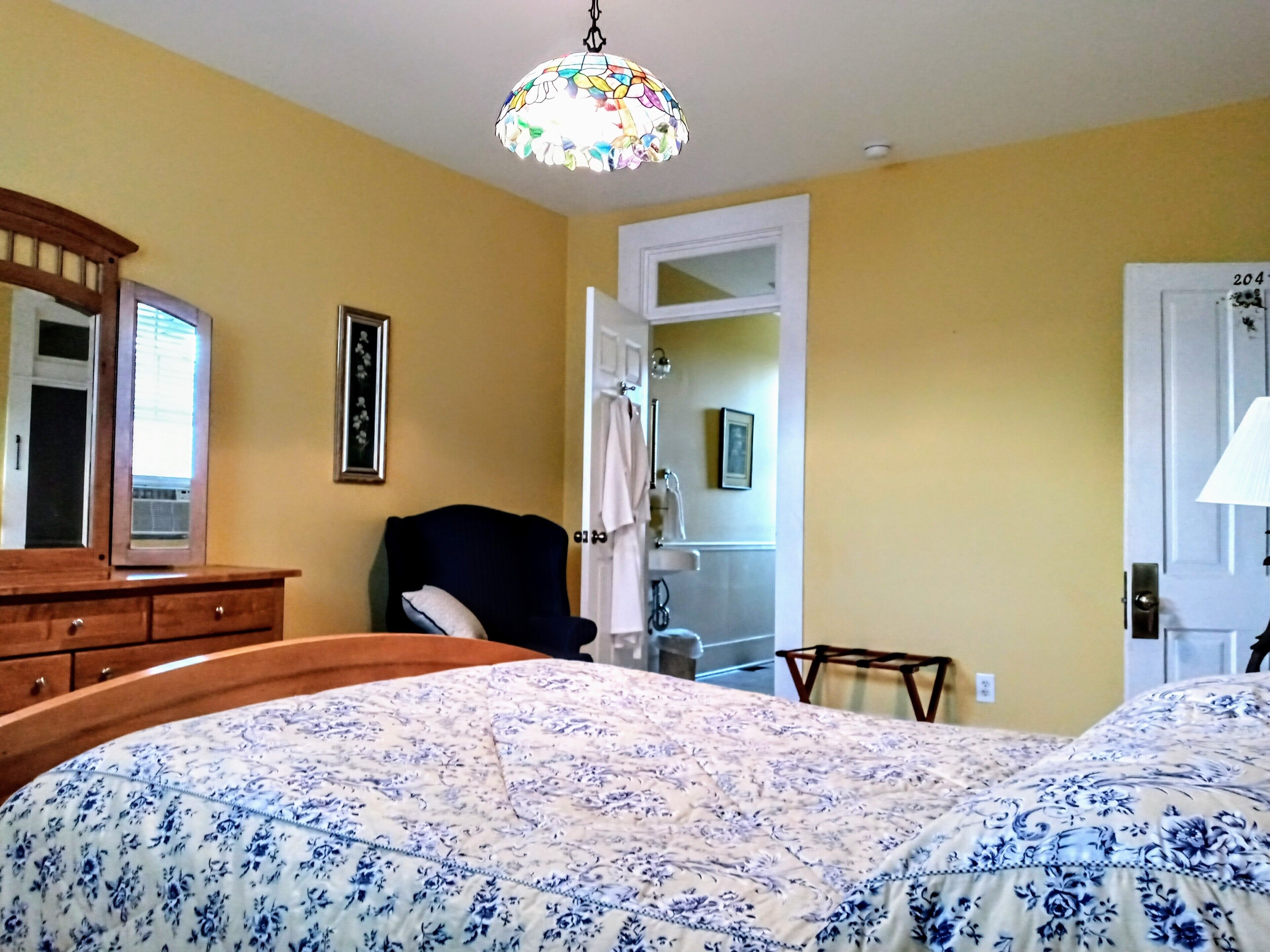 Een slaapkamer met een bed, een stoel, een dressoir en een deur naar een badkamer.