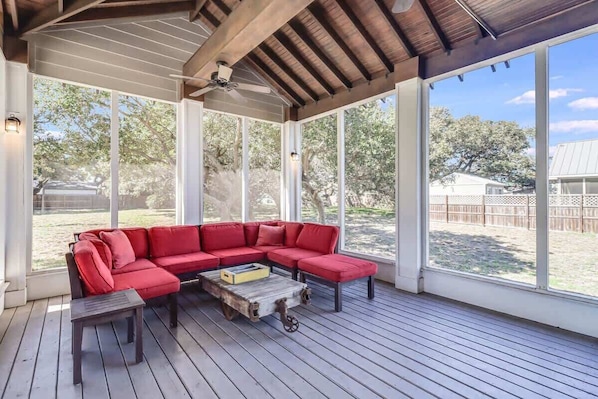 Un espace extérieur aménagé, abrité et doté d’un canapé d’angle rouge, d’une table basse en bois et de grandes fenêtres donnant sur le jardin.