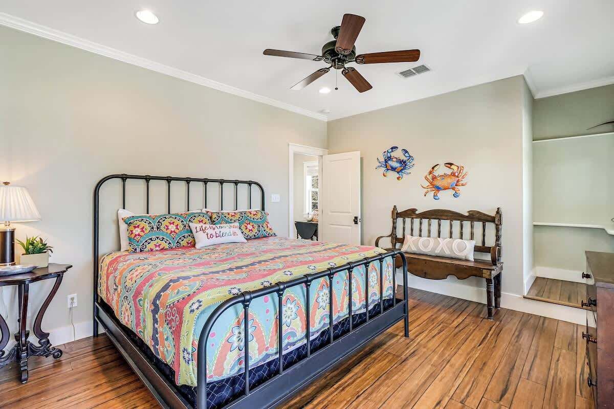 A bedroom with a bed, a ceiling fan, a wooden bench, and a wall decoration.