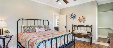 A bedroom with a bed, a ceiling fan, a wooden bench, and a wall decoration.