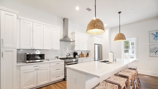 Una cocina moderna con armarios blancos, estufa de acero inoxidable y una isla grande con taburetes de bar.