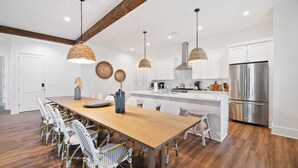 Una cocina moderna con armarios blancos, un refrigerador de acero inoxidable y una mesa de comedor de madera con sillas de mimbre.