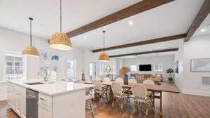 Cocina amplia con isla central, armarios blancos y lavavajillas. Hay sillas de mimbre y una mesa de comedor con ventilador.