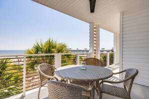 Ein Balkon mit Korbmöbeln, einem Glastisch und Blick auf Strand und Meer.