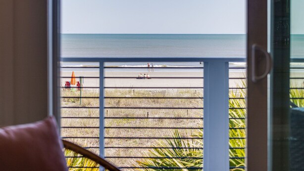 Blick vom Balkon auf einen Strand mit ein paar Personen und Liegestühlen.