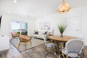 A modern living room with a wooden dining table, wicker chairs, and a ceiling fan.