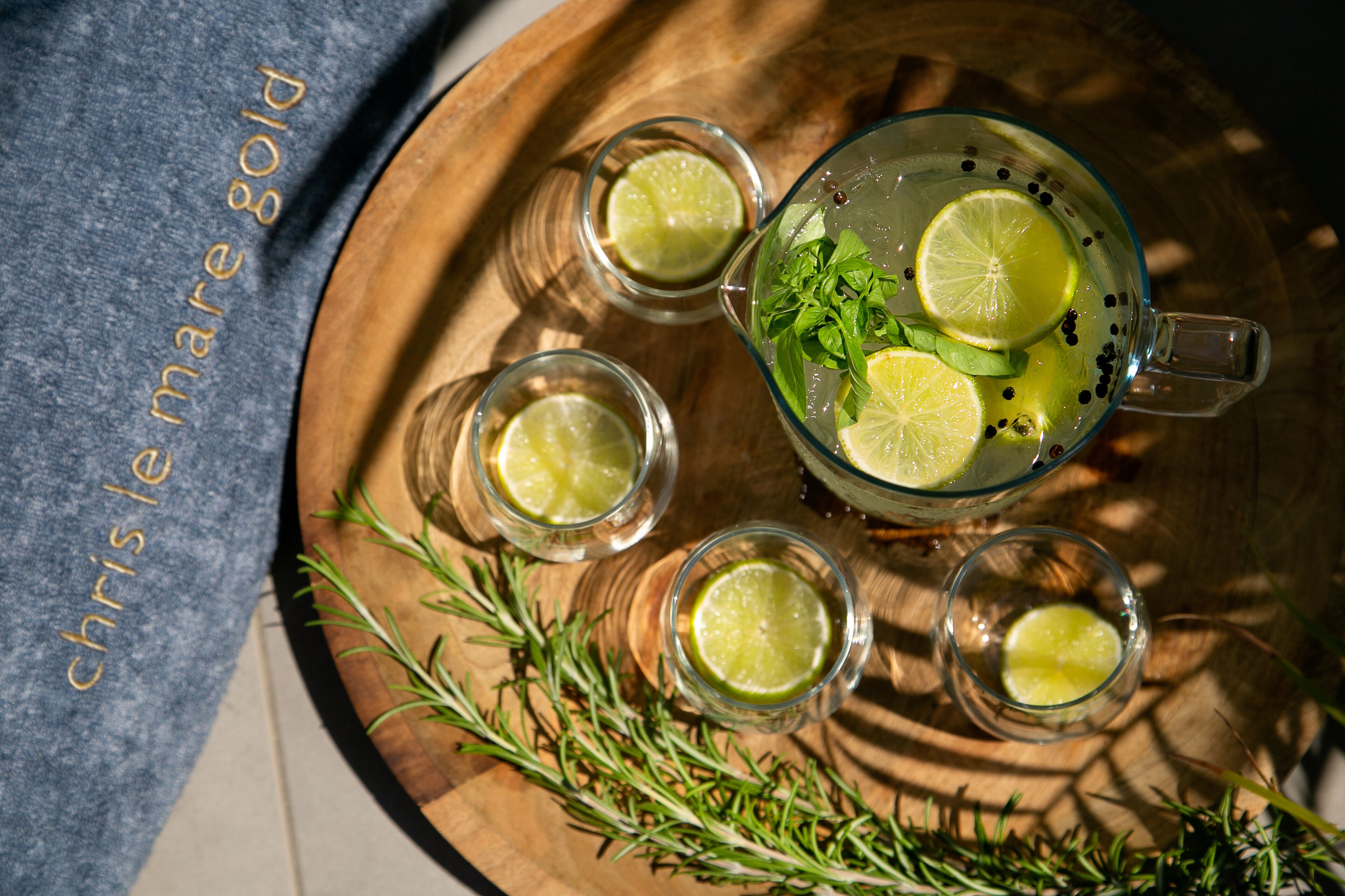 A glass pitcher with lime slices and mint, surrounded by four small glasses with lime slices, all on a wooden tray.