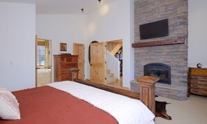 A bedroom with a large bed, a stone fireplace, a wooden dresser, and a mirror.