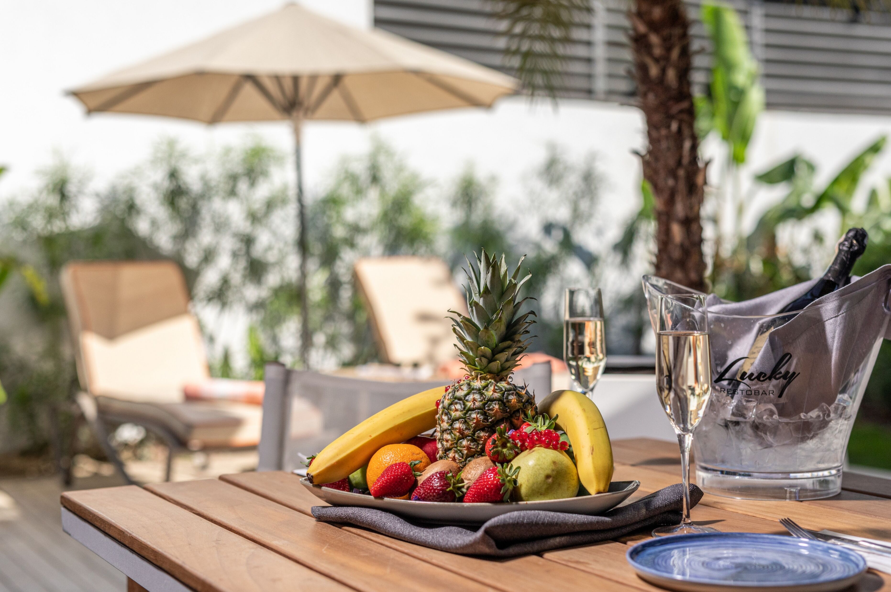 Una mesa de madera con una bandeja de frutas, una copa de champán y una botella de Lucky champagne.