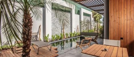 An outdoor patio with wooden tables and chairs, a palm tree, and a stone wall.