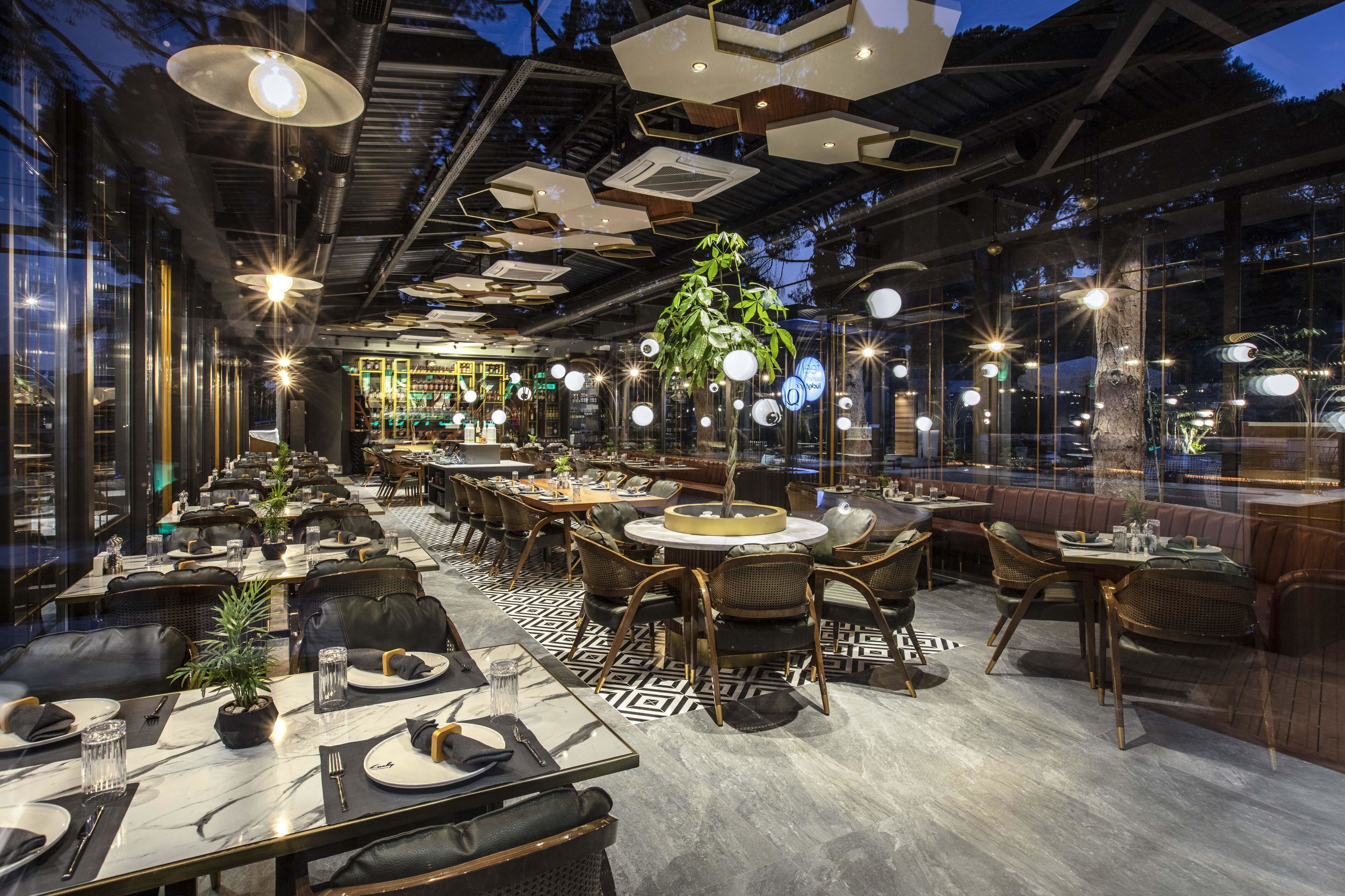 Ein modernes Restaurant mit runden Tischen, schwarzen Ledersesseln und hängenden Pflanzen.
