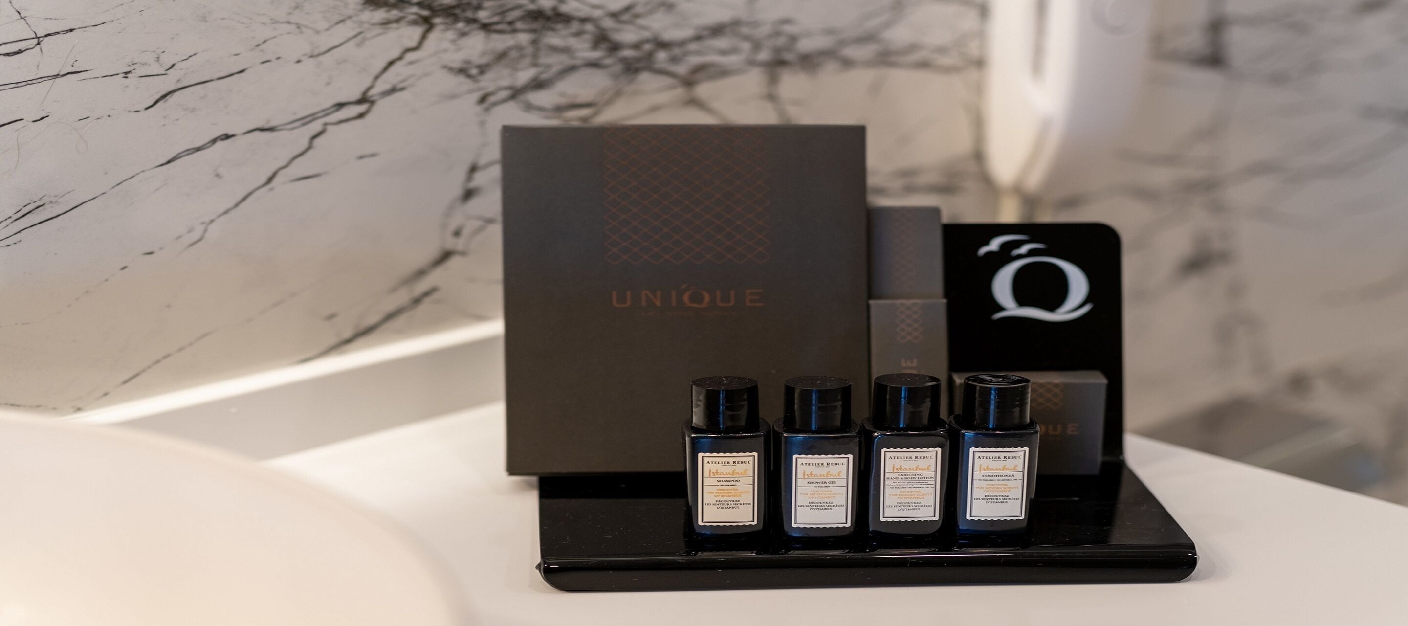 A display of four black bottles with labels, a black box with 'UNIQUE' written on it, and a black stand with a white 'Q' logo.