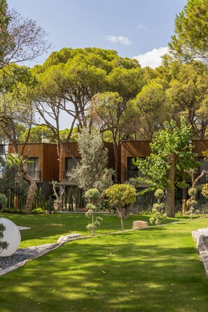 A modern building with a wooden facade, surrounded by a well-maintained garden with various trees and shrubs. - Unique Life Style Hotel (Kusadasi)