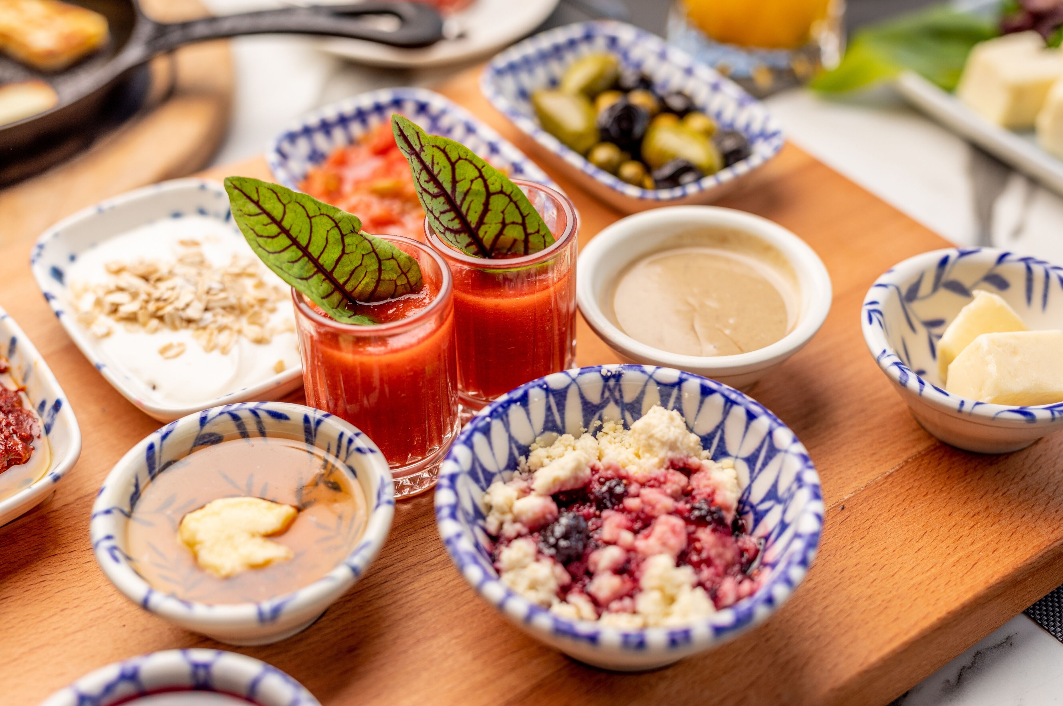 A wooden table with various bowls of food, including a bowl of mixed berries, a bowl of yogurt, and a bowl of soup.