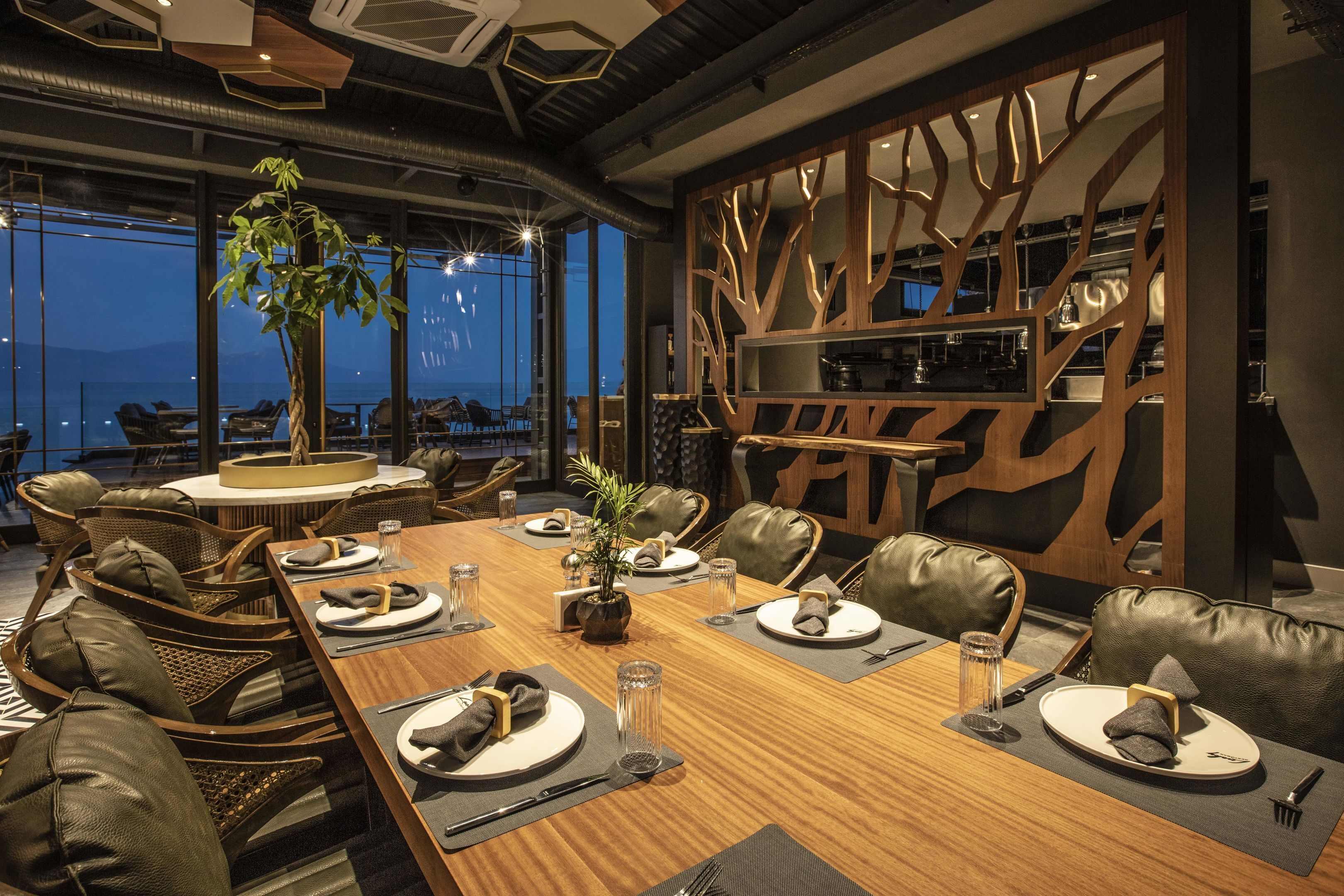 A dining area with a wooden table set for a meal, leather chairs, and a large window offering a view of the outdoors.