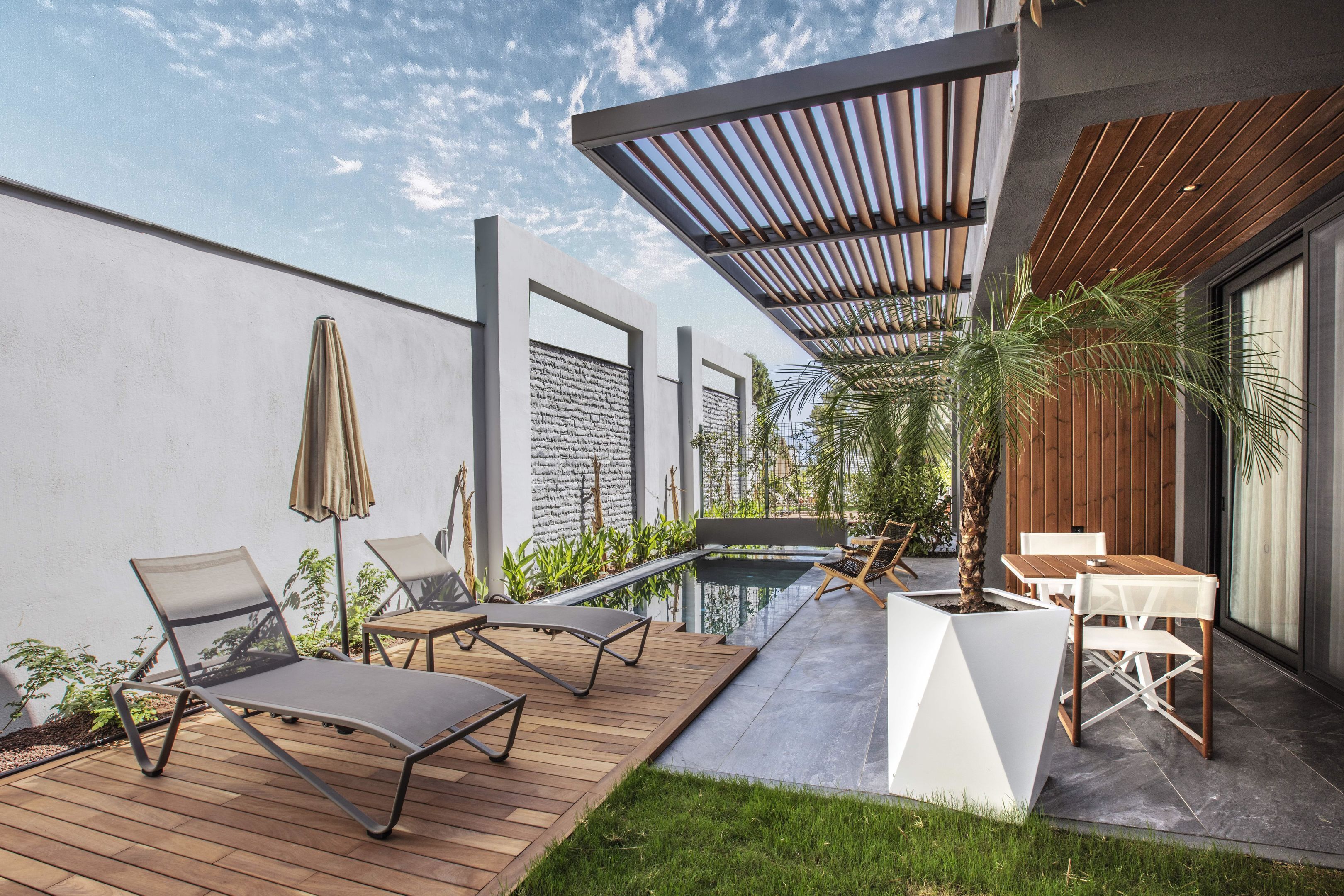 A modern outdoor patio with a pool, lounge chairs, and a wooden pergola.