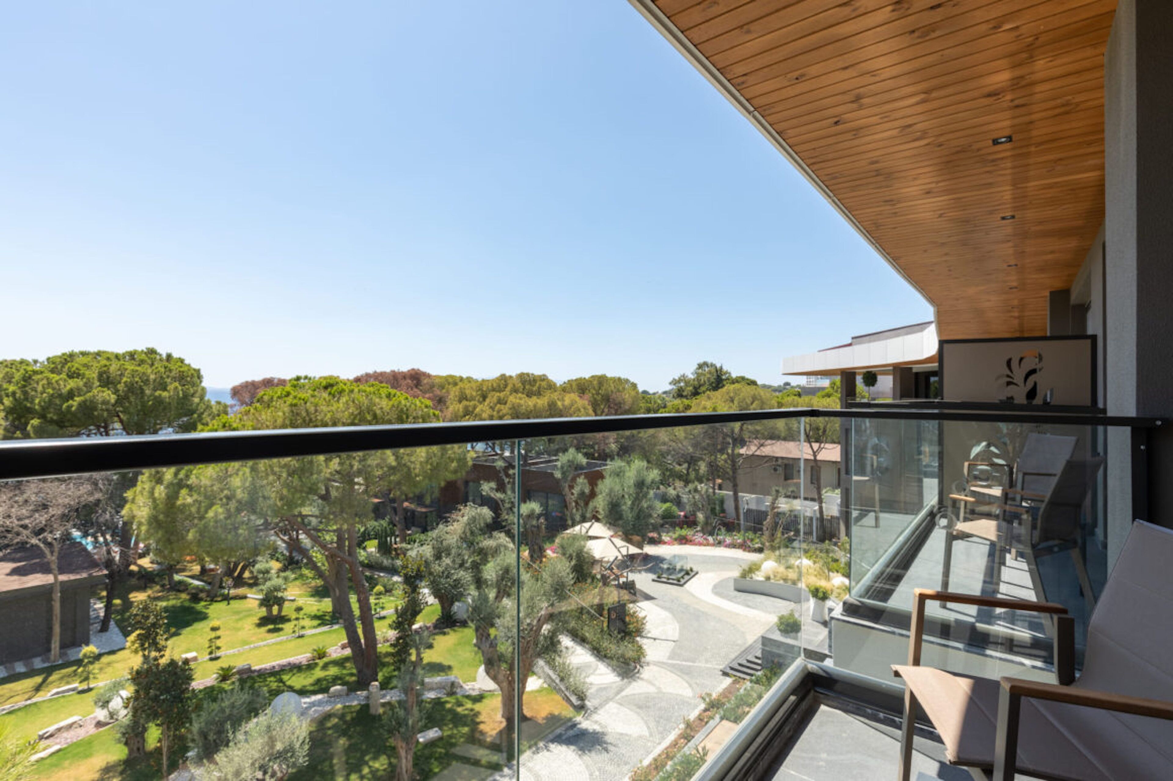 A modern building with a glass balcony overlooking a landscaped garden and distant trees.