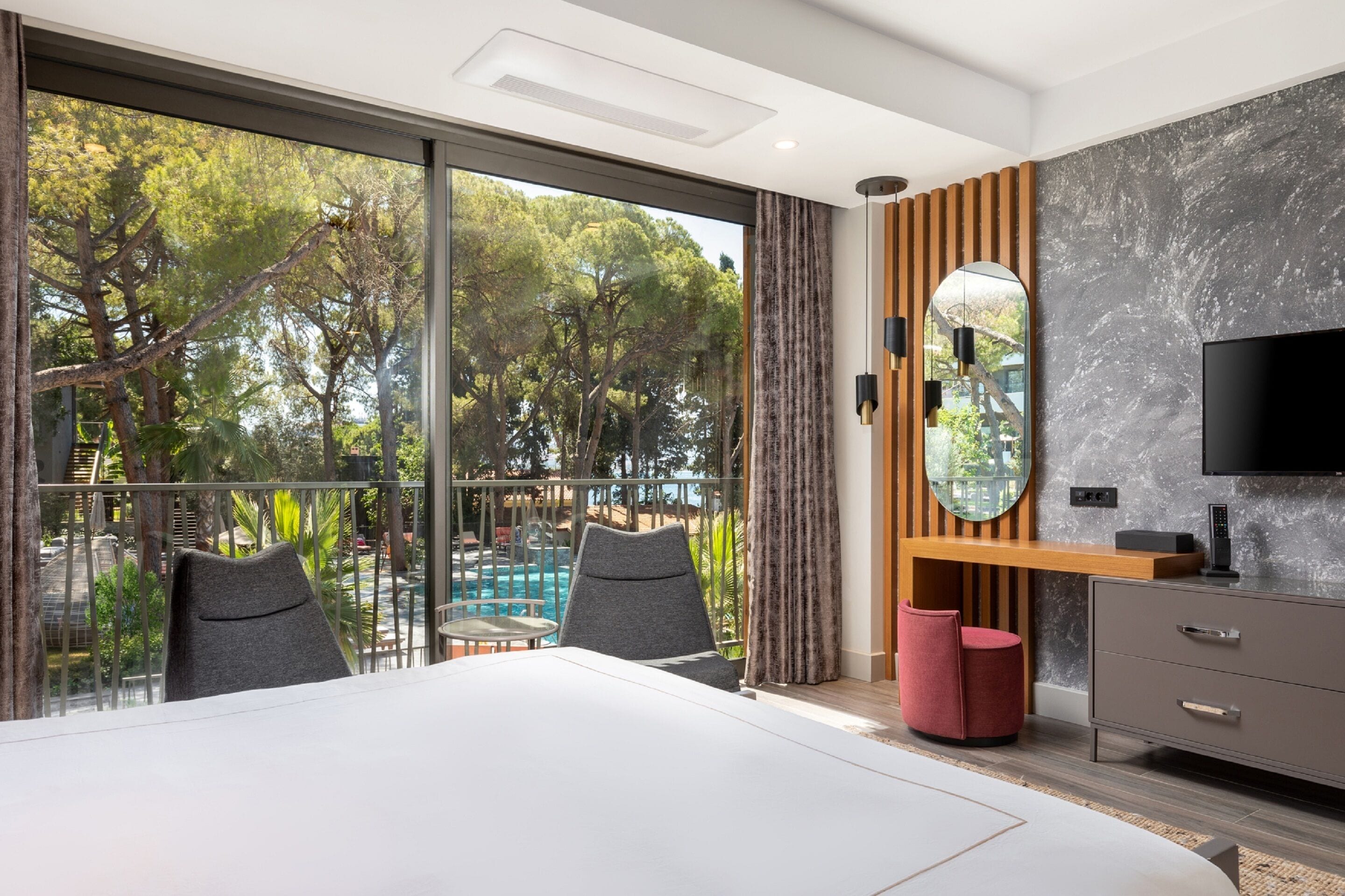 Camera d'albergo moderna con una grande finestra, un letto, una TV e una scrivania in legno.