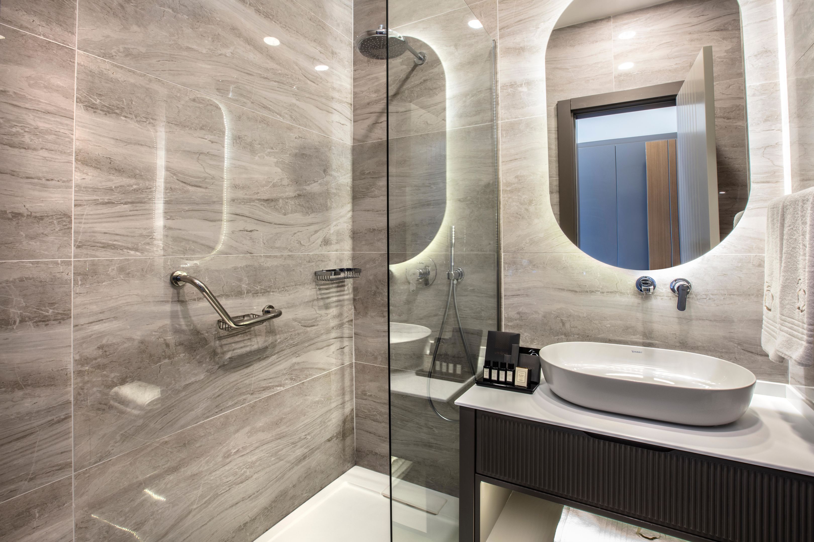 A modern bathroom with a glass-enclosed shower, a white sink, and a mirror above it.