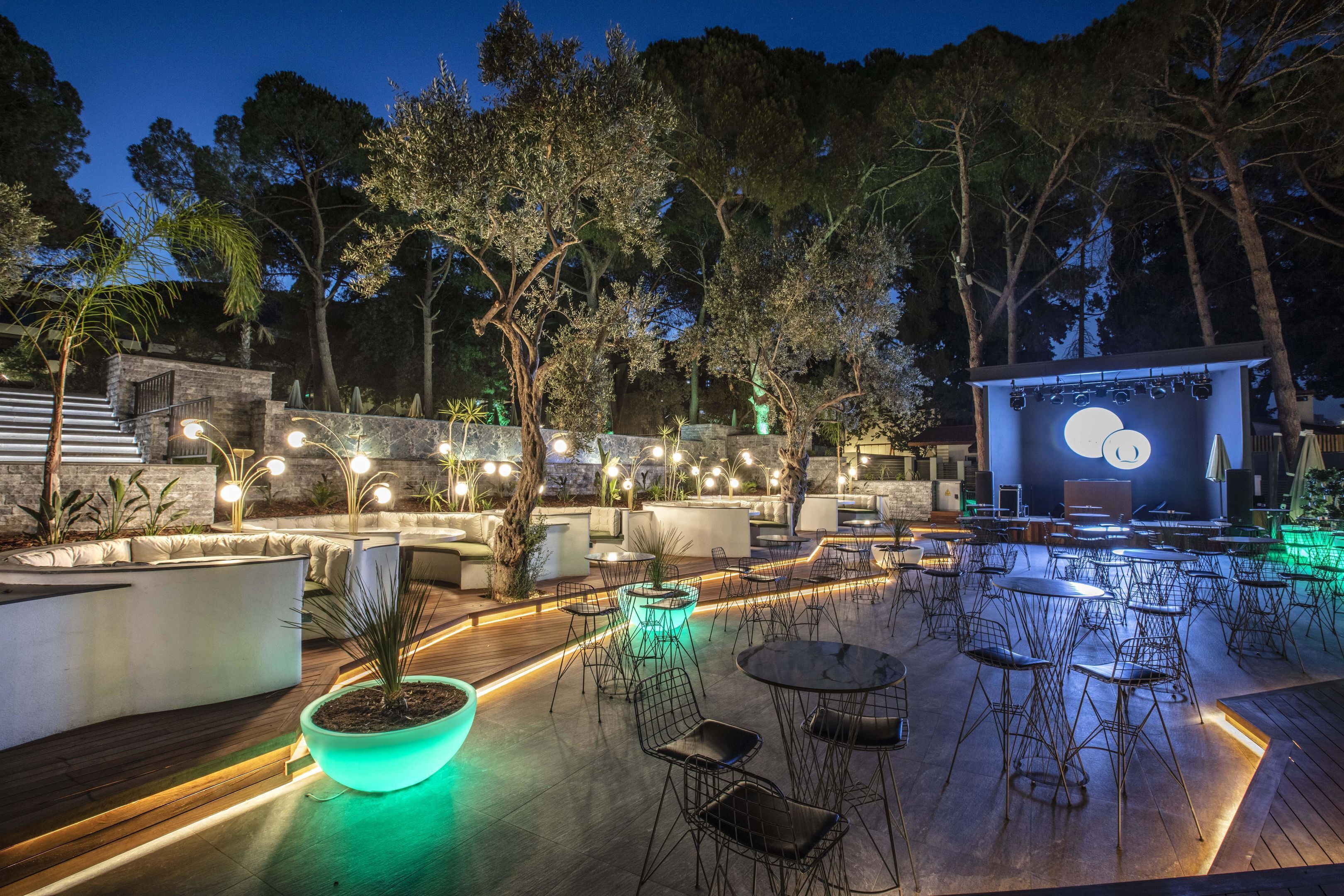 An outdoor patio area with seating and tables, surrounded by trees and a stage with a moon design.