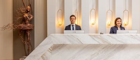 A reception desk with two staff members, a marble counter, and a unique sculpture.