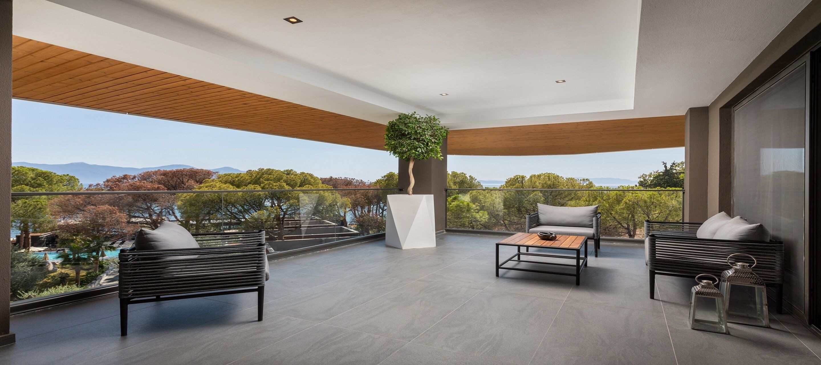 Un balcón amplio con muebles modernos, una planta en maceta y vistas a montañas y árboles.