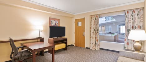 A hotel room with a wooden desk, a television, a sofa, and a window with curtains.