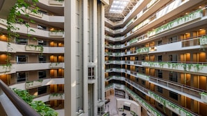 Un atrio de varios niveles con balcones, plantas de interior y un espacio abierto central con asientos.