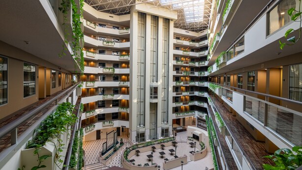 Un atrio de varios niveles con un espacio central abierto, balcones con plantas y un diseño arquitectónico moderno.