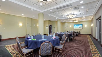A conference room with round tables, chairs, and a large screen displaying a beach scene.