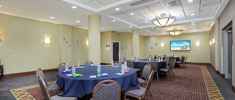 A conference room with round tables, chairs, and a large screen displaying a beach scene.