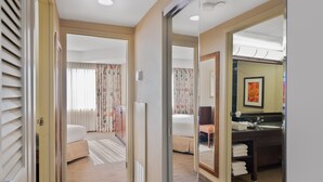 Habitación de hotel con cama, baño con lavabo y espejo, y una puerta que da a otra habitación.