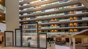 Un vestíbulo de hotel de varios niveles con una fuente central, múltiples balcones con plantas y una zona de recepción.