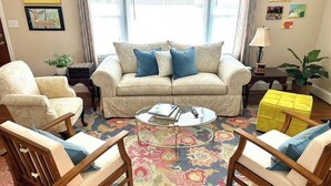 Ein Wohnzimmer mit beiger Couch, zwei Sesseln, einem Couchtisch und einem gemusterten Teppich.
