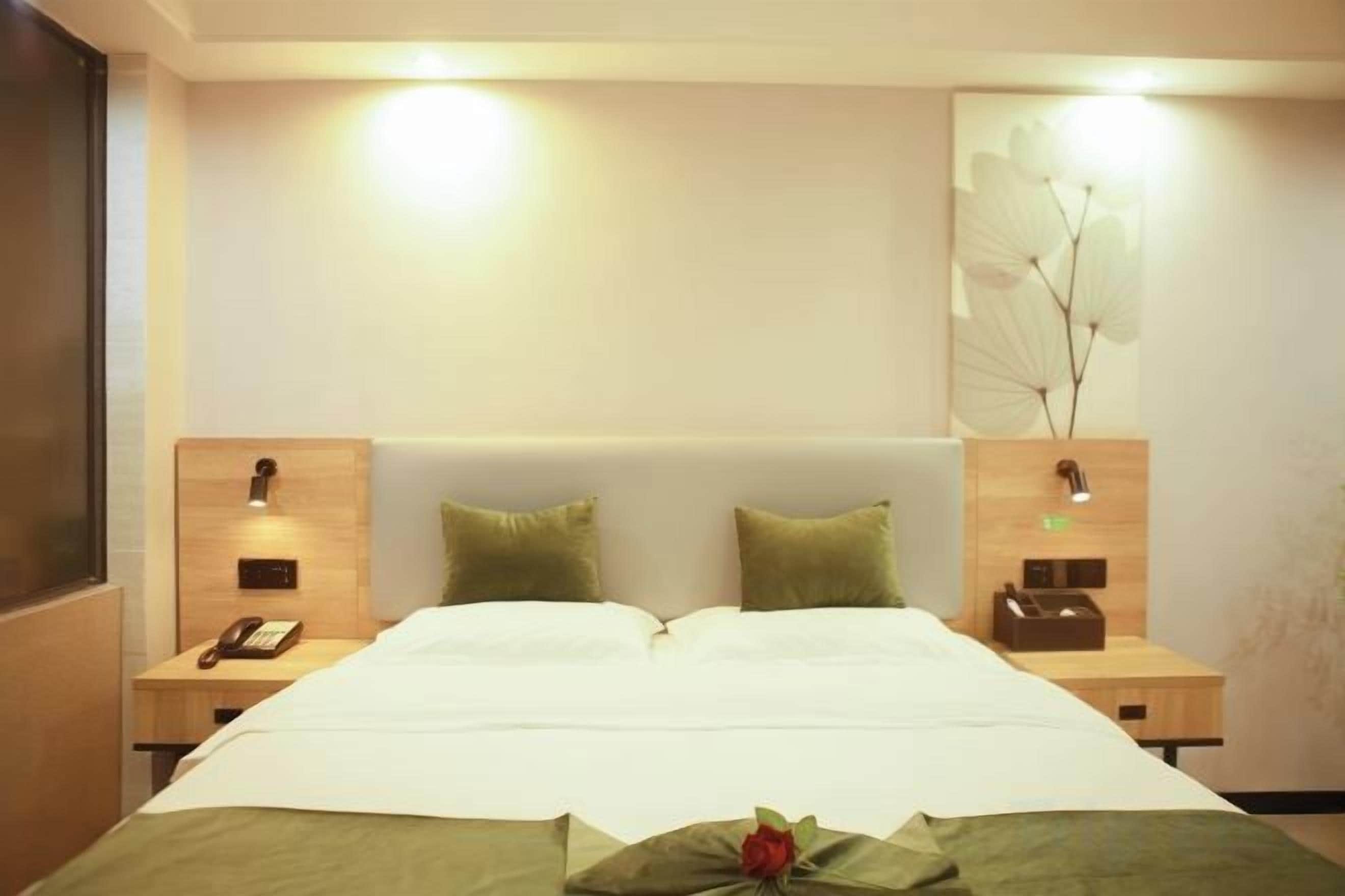 Quarto de hotel com uma cama grande, duas mesas de cabeceira, um criado-mudo e uma luminária de parede.