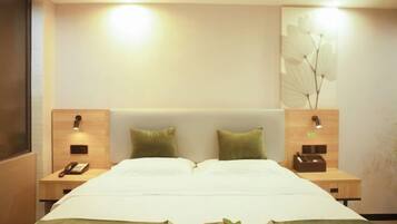 Quarto de hotel com uma cama grande, duas mesas de cabeceira, um criado-mudo e uma luminária de parede.