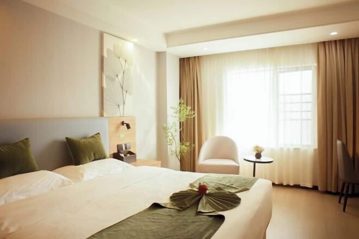 Hotellihuone, jossa on suuri sänky, pieni pöytä, tuoli ja ikkuna, jossa on verhot.