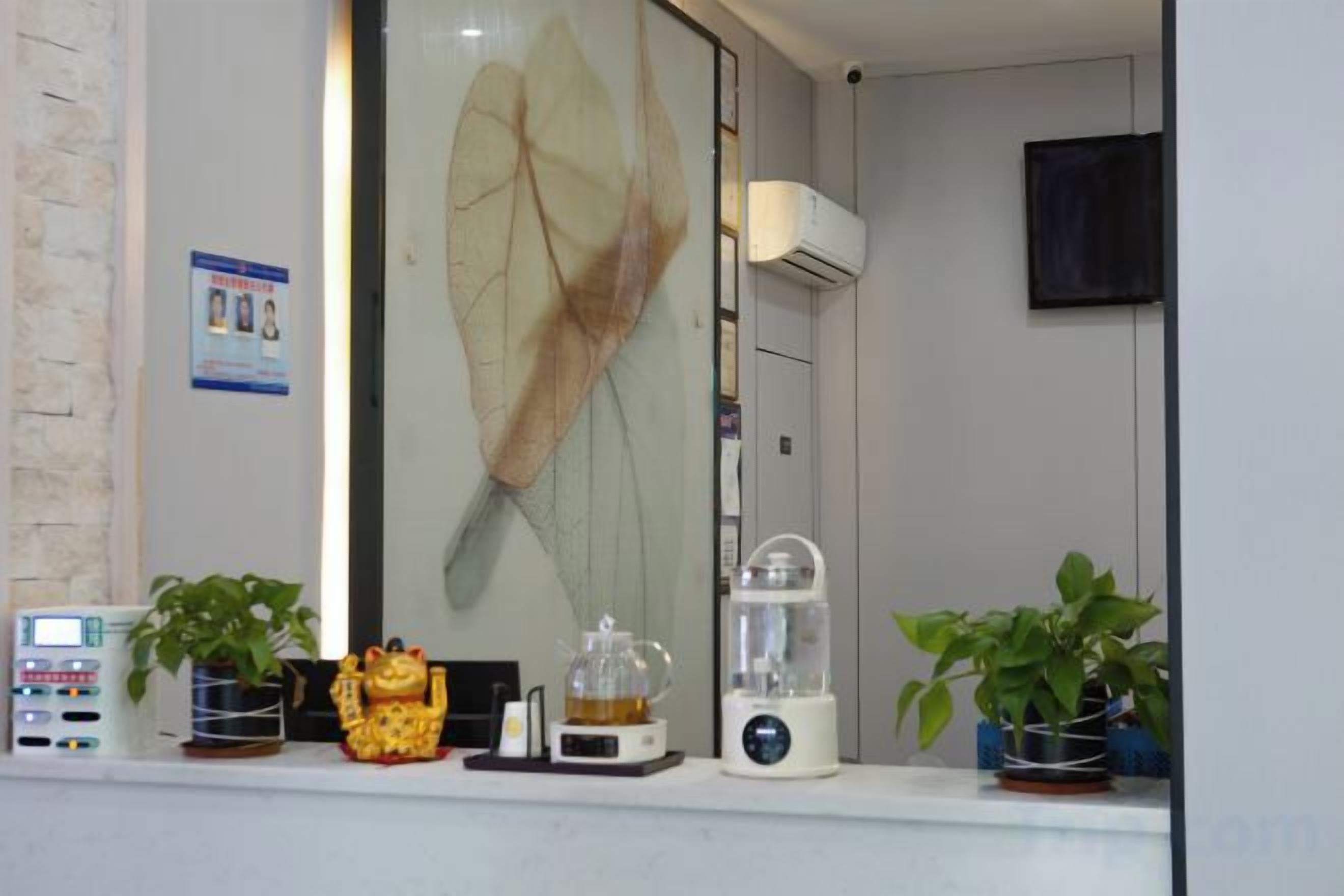 A room with a large window, a wall-mounted air conditioner, a television, and a shelf with various items including a plant, a decorative item, and a blender.