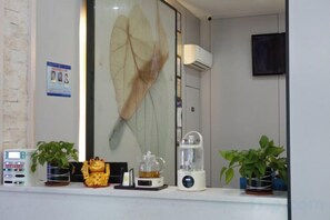 Une pièce dotée d’une grande fenêtre, d’un climatiseur mural, d’un téléviseur et d’une étagère sur laquelle se trouvent divers objets, notamment une plante, un objet décoratif et un mixeur.