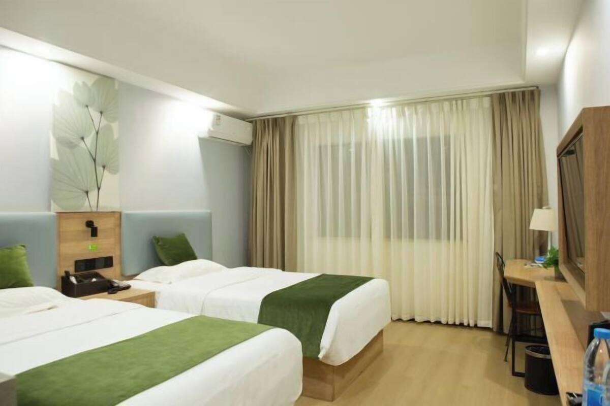 Hotellihuone, jossa on kaksi sänkyä, työpöytä, tuoli, lamppu ja suuri ikkuna, jossa on verhot.
