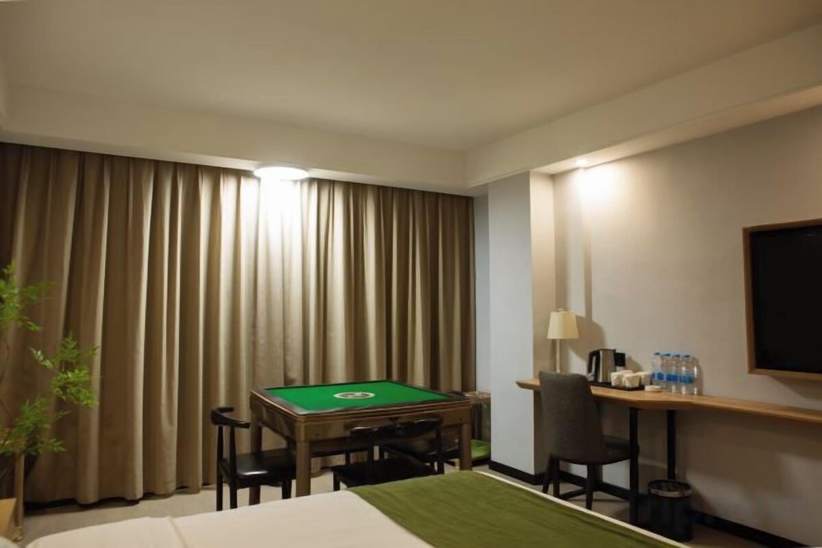 Habitación de hotel con mesa de billar verde, cama, escritorio con lámpara y televisor.
