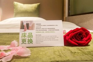 A hotel room with a bed, a red rose, and a card on the bed. - GreenTree Inn Express Hotel (Haikou Haixiu Middle Road Bangbaihui City Branch) (Haikou)