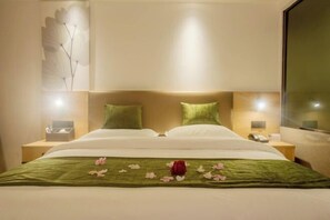 A hotel room with a bed, green pillows, a bedside table with a phone, and a wall-mounted artwork. - GreenTree Inn Express Hotel (Haikou Haixiu Middle Road Bangbaihui City Branch) (Haikou)