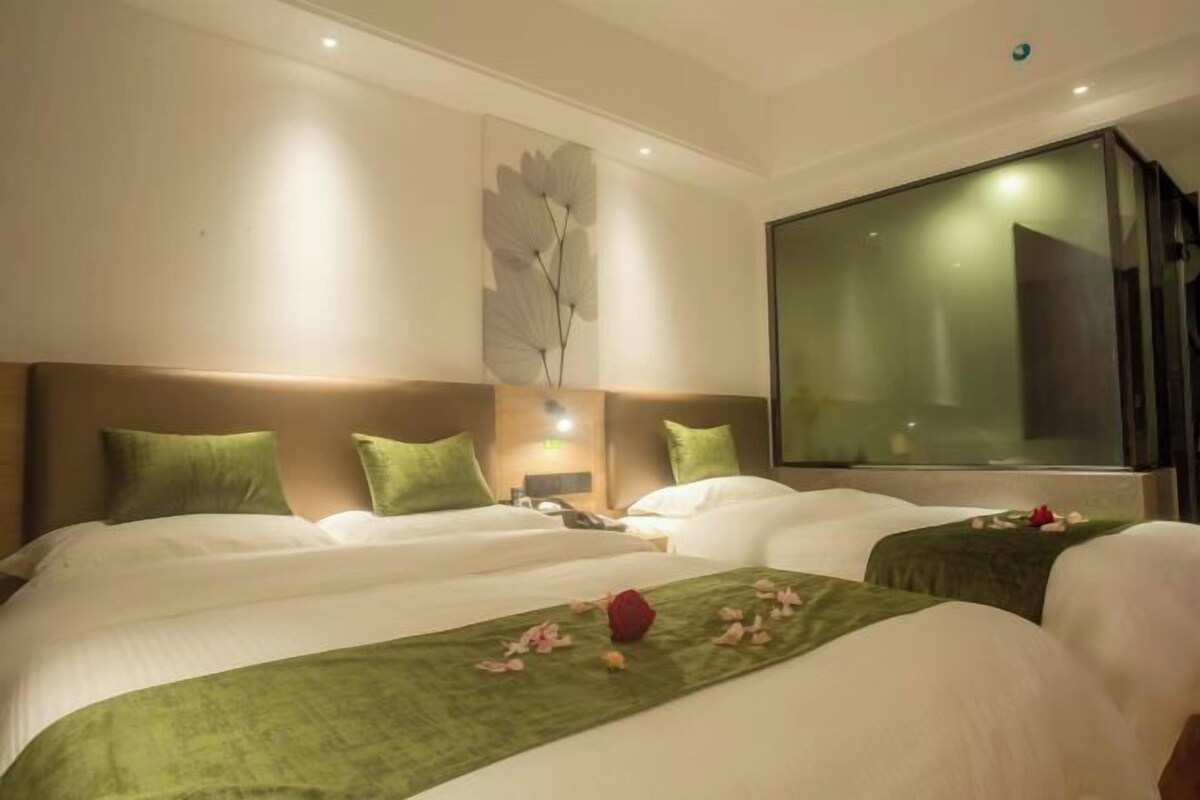 A hotel room with two beds, green bedding, a large window, and a wall-mounted artwork.