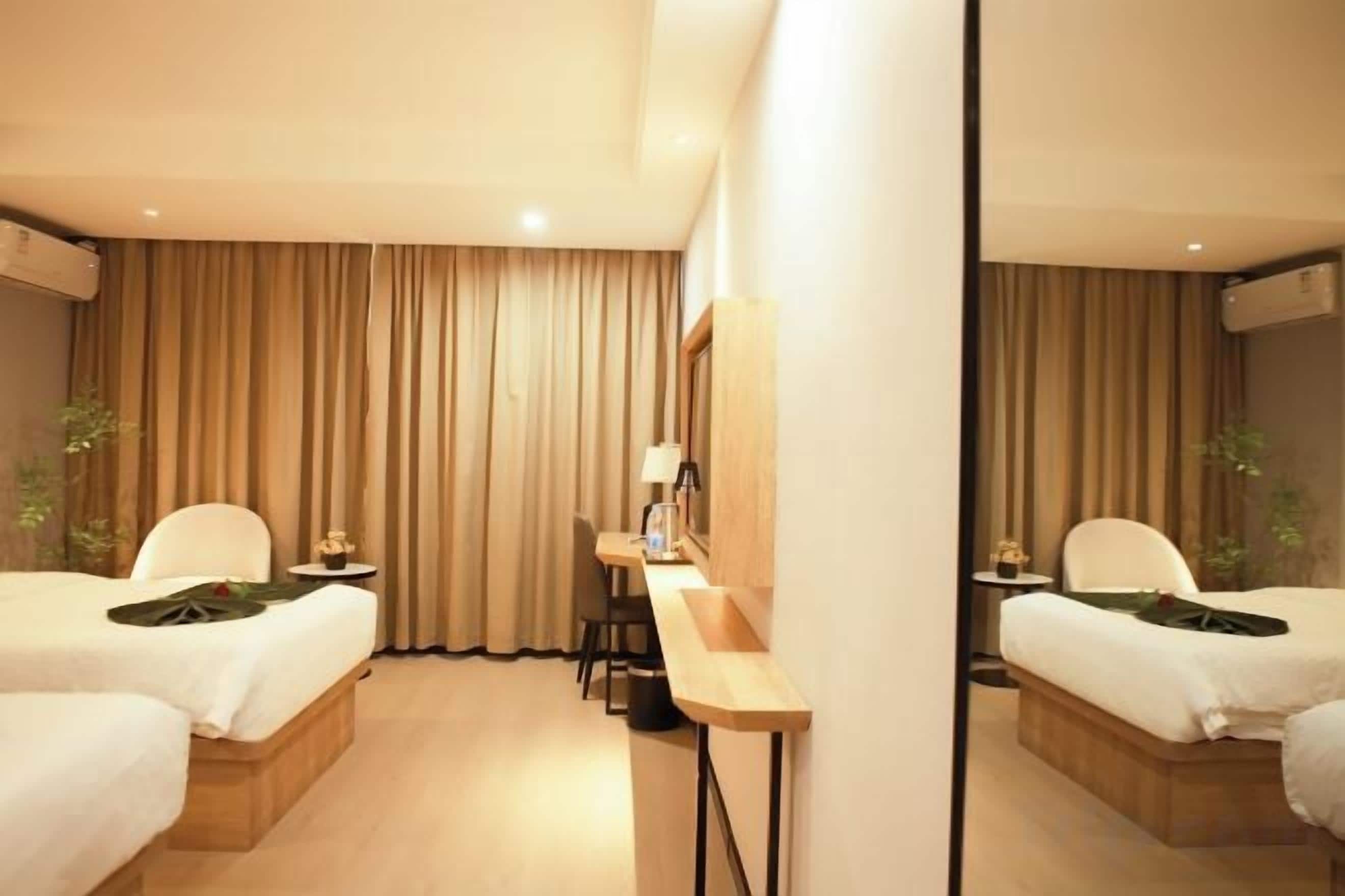 A hotel room with two beds, a desk, and a mirror.