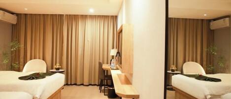 A hotel room with two beds, a desk, and a mirror.