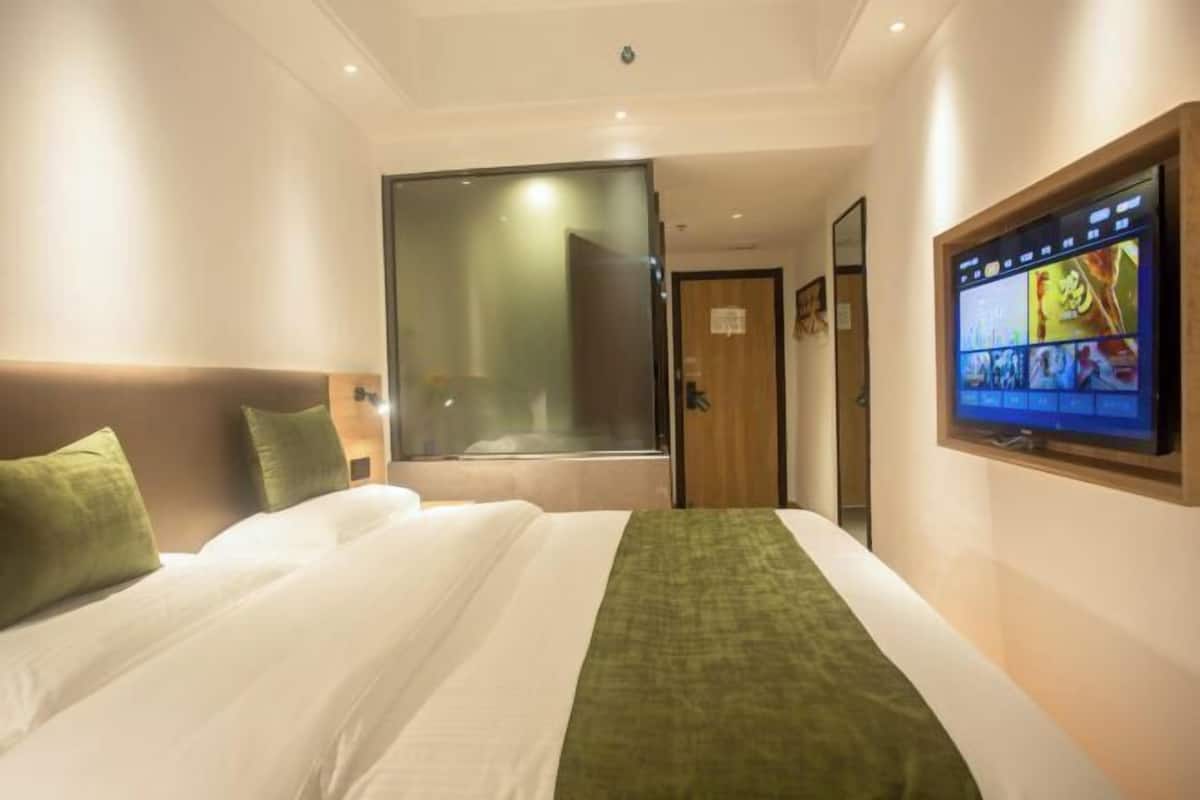 Hotellihuone, jossa on suuri sänky, seinälle asennettu televisio ja liukuovi, joka johtaa kylpyhuoneeseen.