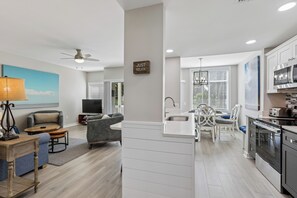 Een moderne keuken met een centraal eiland, een eethoek met tafel en stoelen, en een woonkamer met een bank en een televisie.